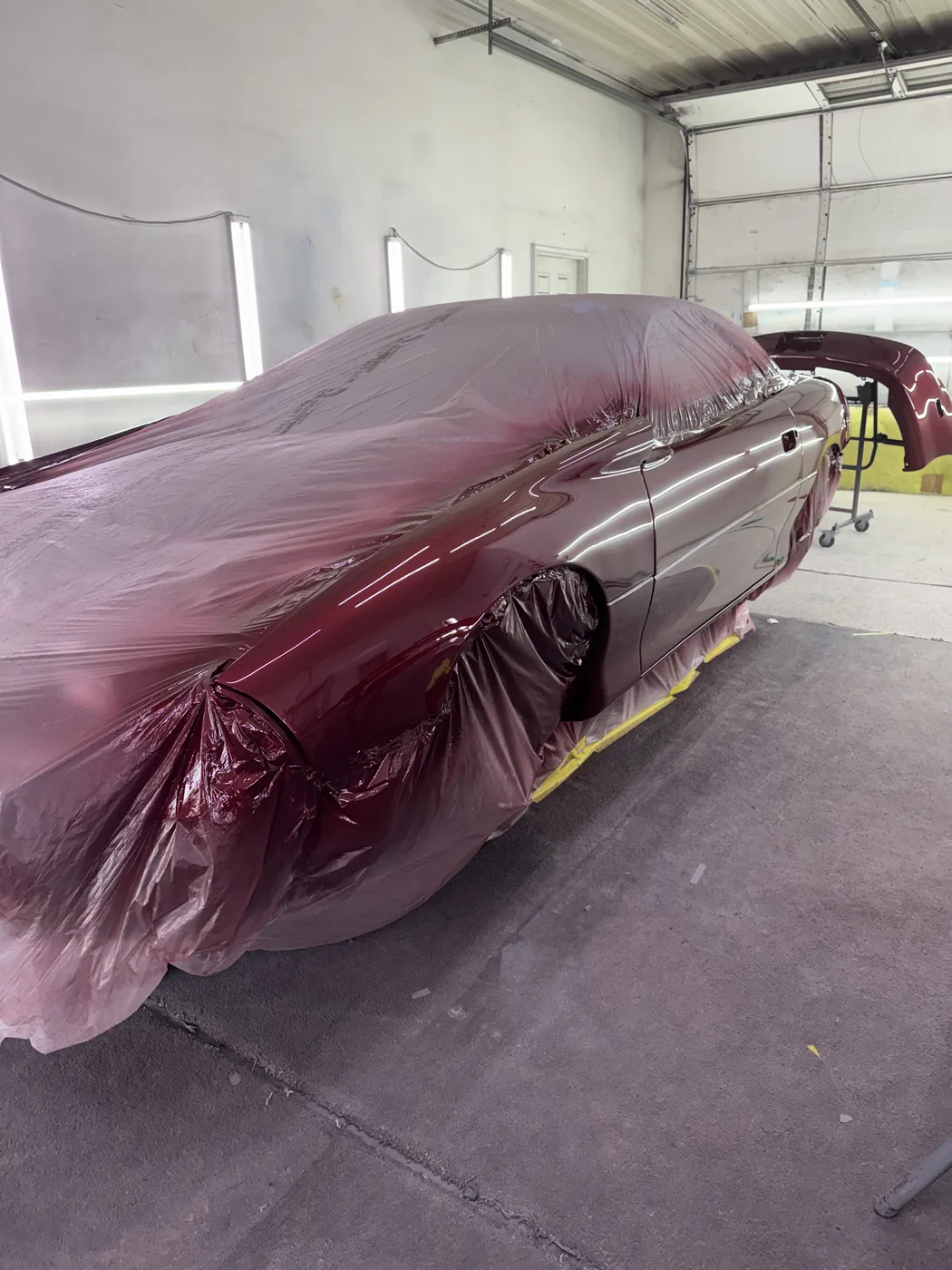 Burgundy vehicle masked inside the shop for refinishing
